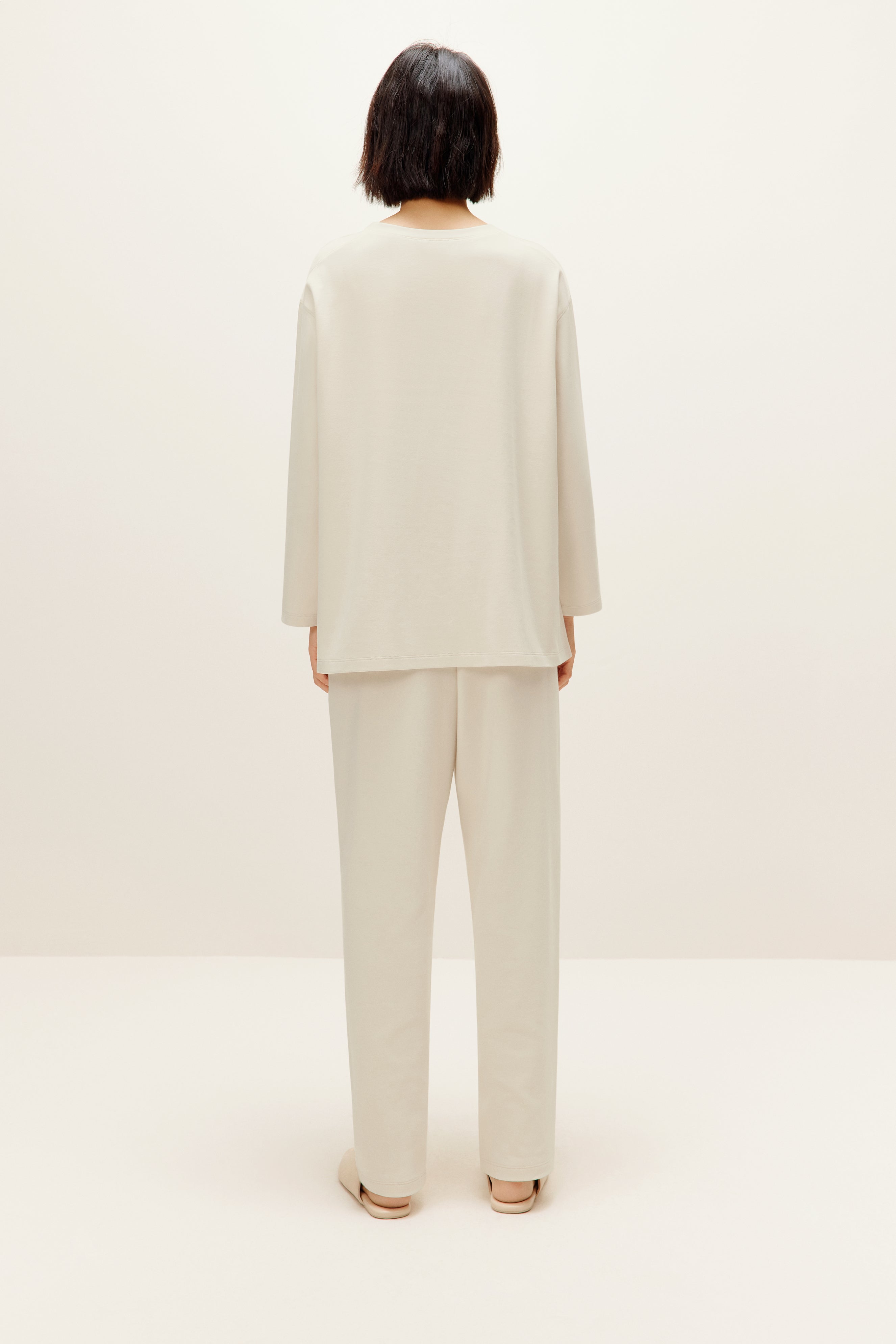 a woman wearing a cream color pull over top and pants from back