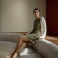 A woman wearing green pajamas and a white knitted sweater sits on a white couch.