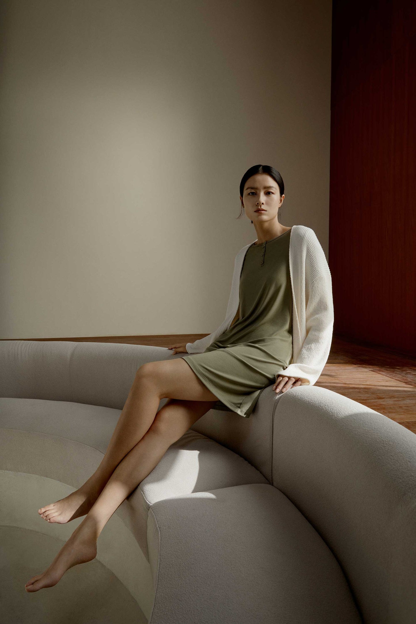 A woman wearing green pajamas and a white knitted sweater sits on a white couch.
