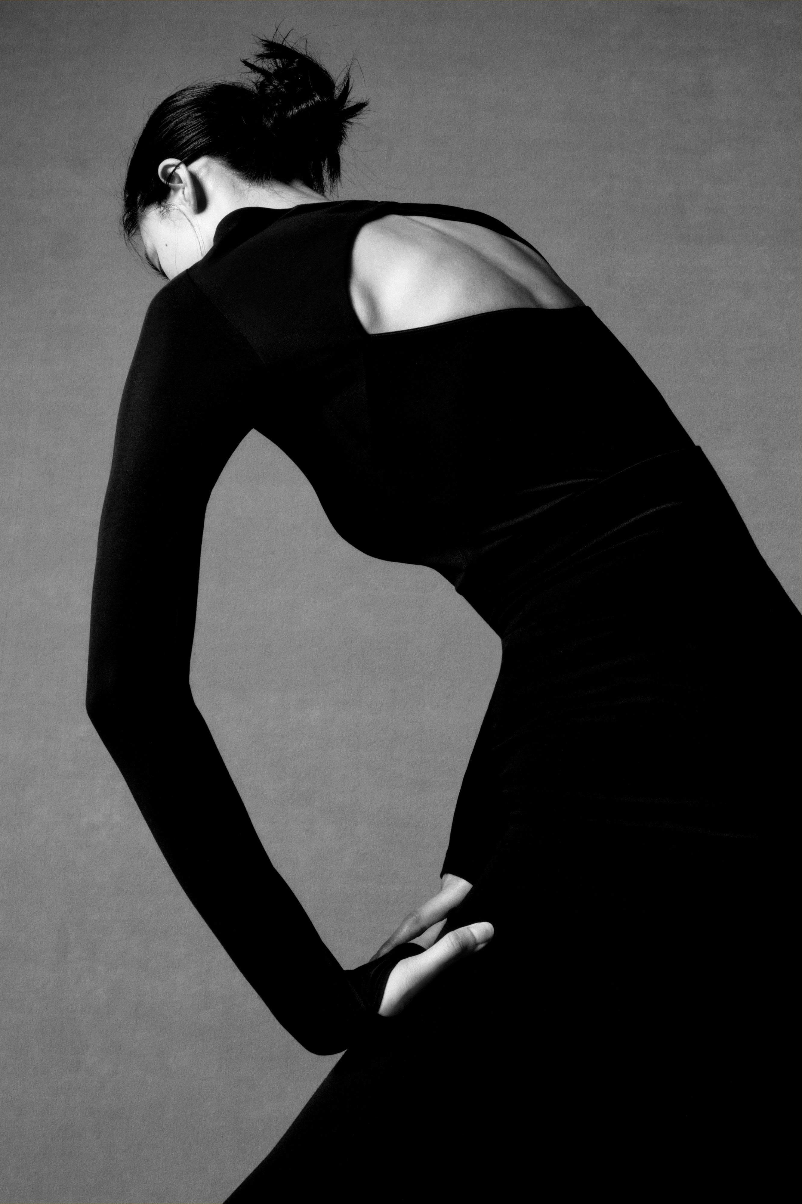 back of woman in black long sleeve top and midi skirt