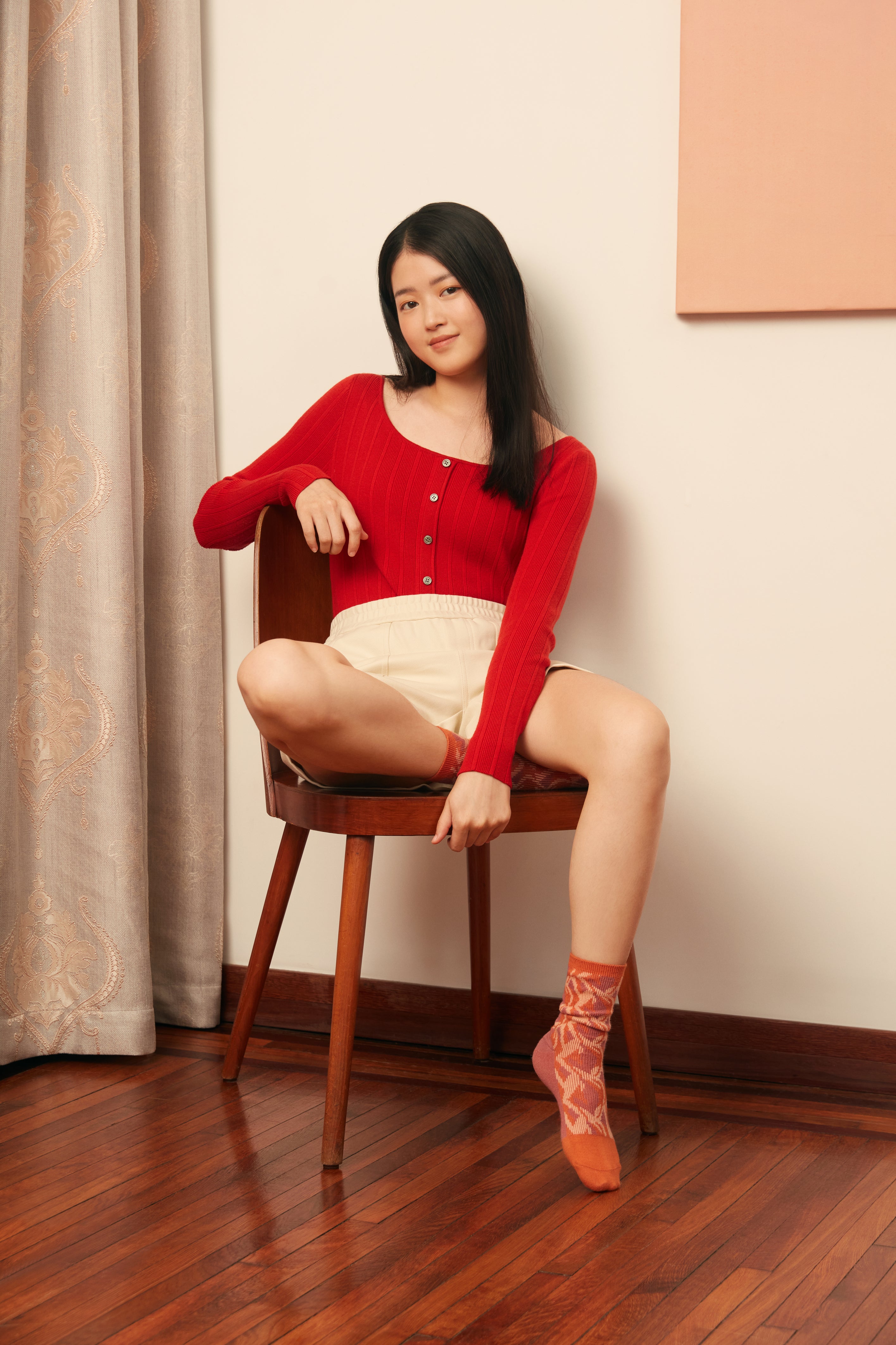 woman sitting in red cardigan and white shorts