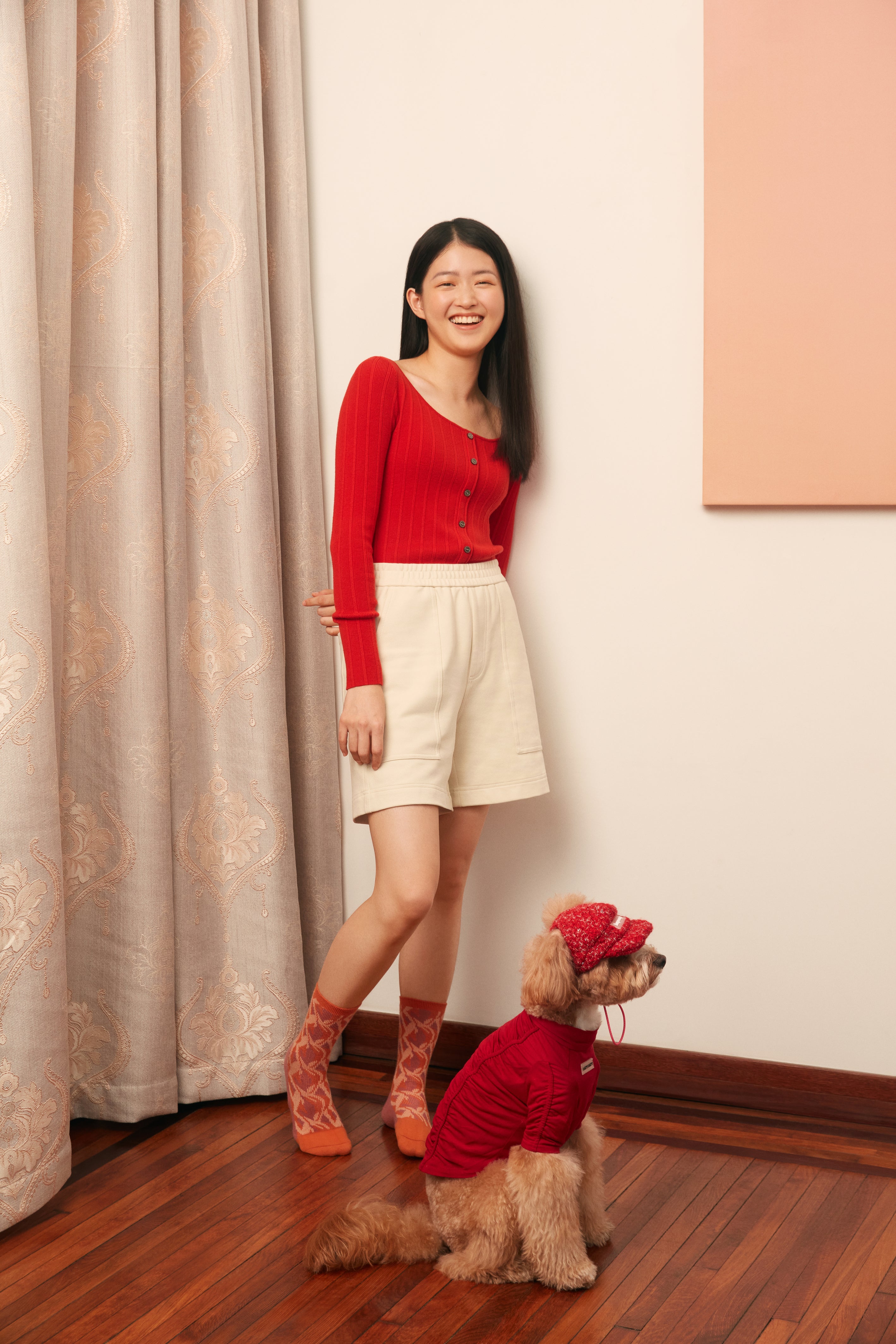 woman in golden yellow cardigan and white shorts standing with a dog in red clothes